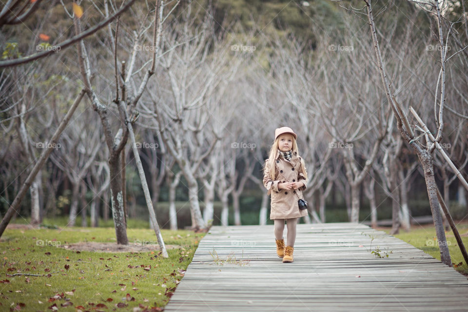 Cute little girl with blonde hair walking in autumnal park