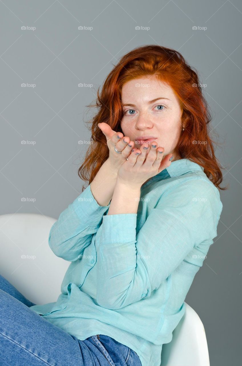 Lifestyle portrait of beautiful, cute, attractive redhead woman with freckles, blue eyes, curly hair sitting in the arm chair. Natural beauty
