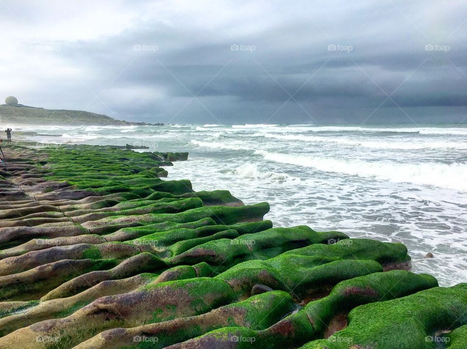 Geological park in Taiwan. Green seaweed/algae growing on the rocks. Sea waves hammering against the rocks carving out ridges.