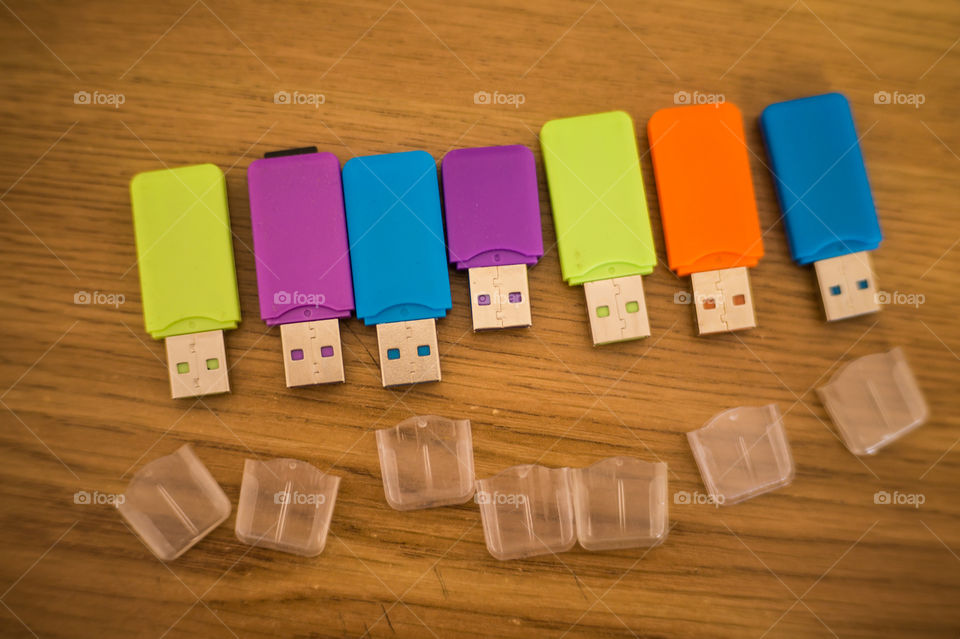 Multi-colored flash drives for working with documents, saving and transmitting, sharing files on a wooden texture table close-up.