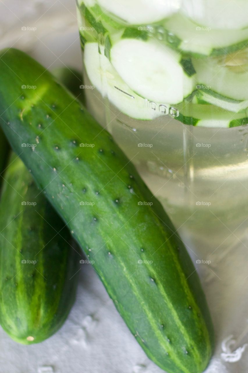 Cucumber-infused water in a half-gallon mason jar with cucumbers on a white dish towel