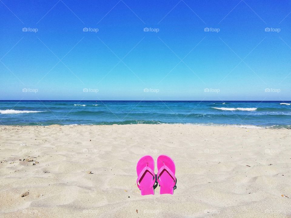 pink flip flops immersed in the sand on the beach