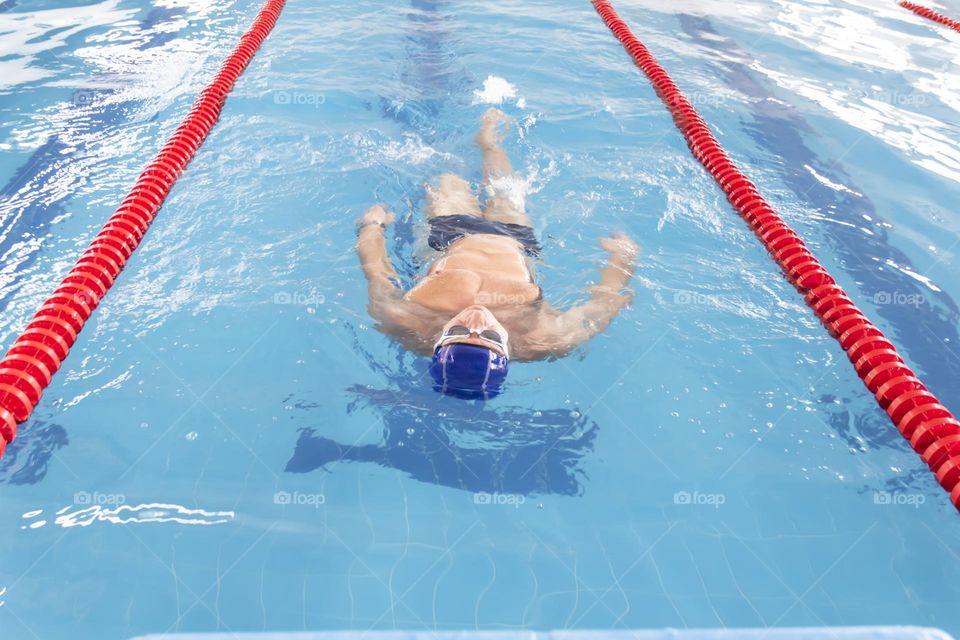 An elderly man is engaged in swimming in the pool to maintain health.