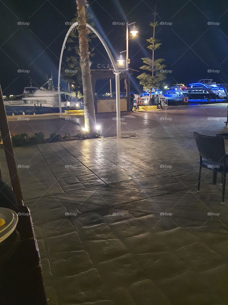 Porto marina egypt The image captures a relaxing nighttime scene at a marina or waterfront area. The warm streetlights and the blue-lit boats create a charming and elegant atmosphere.