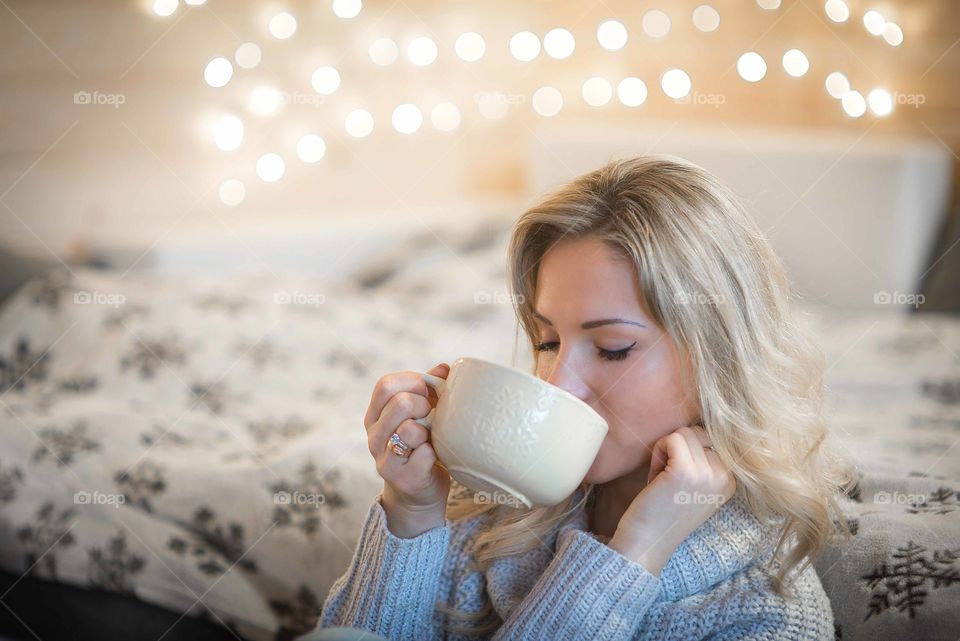 Portrait of a beautiful young woman drinking a cup of hot coffee in winter outfit at home
