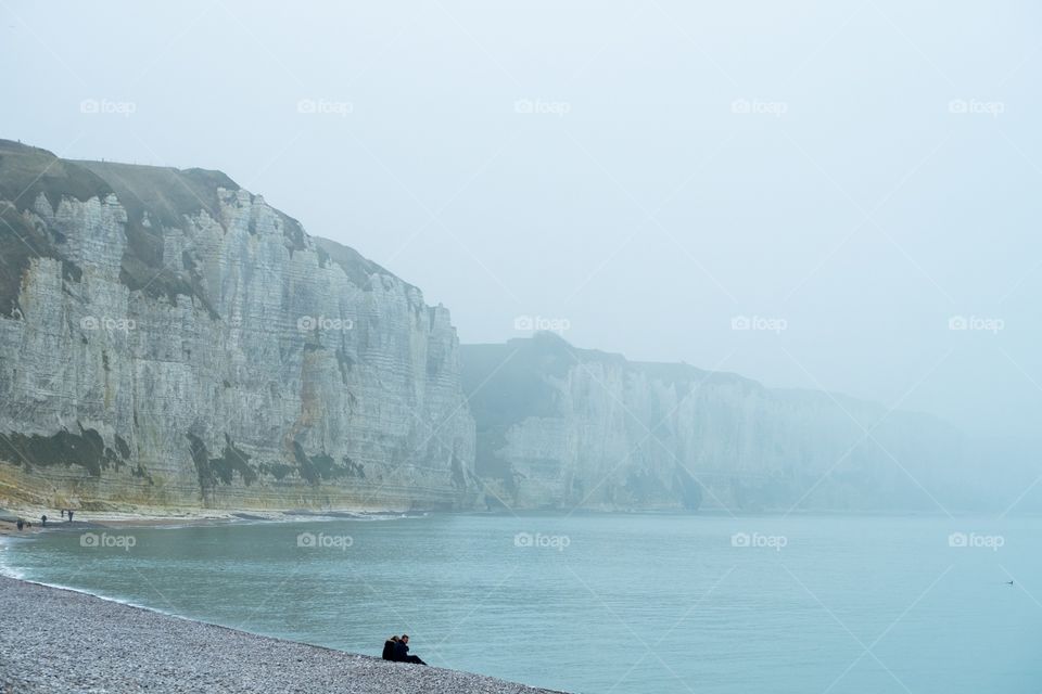 Silhouette of a couple watching over the fading sea from the Foggy beach of Fécamp, Normandy, France  with the white chalk cliffs in the background 