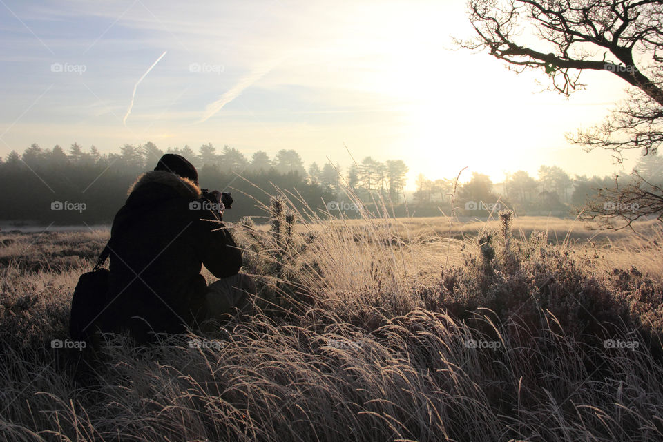 A portrait of a photographer framing a scenic landscape shot of the meadow during golden hour.