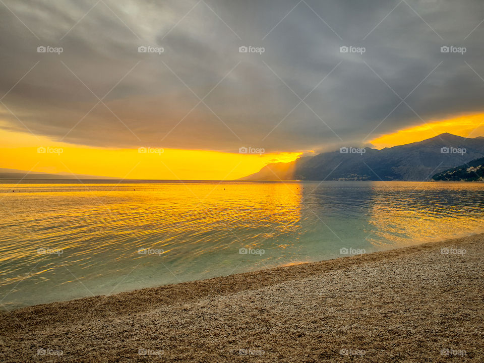 Croatia, Dalmatia, Brela.  A deserted pebble beach with a calm Adriatic Sea amid mountains and bright sunset