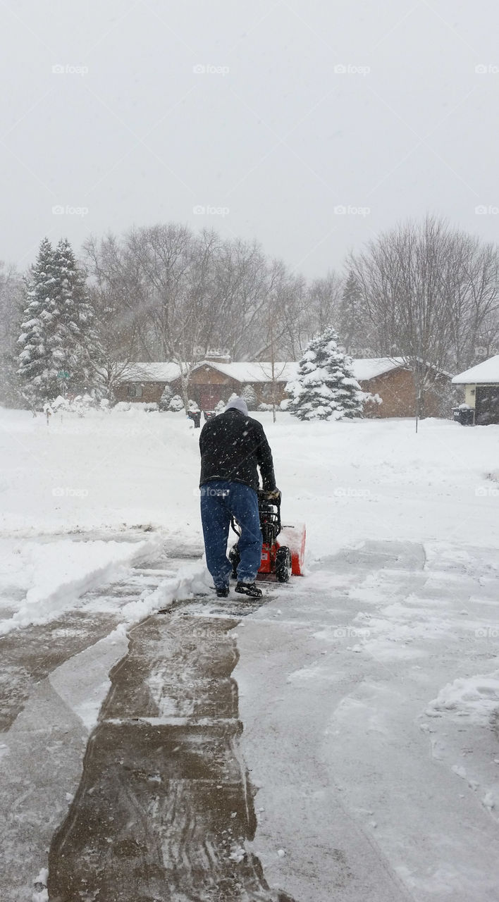 Man snow blowing a drive way in falling snow