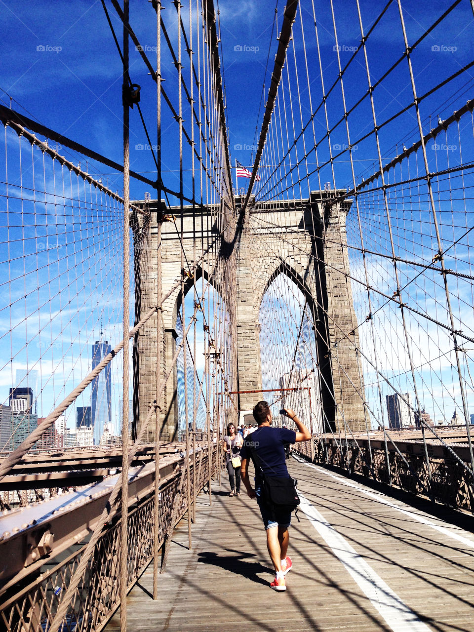 A tourist is taking Photo of everything Walking on the Brooklyn Bridge