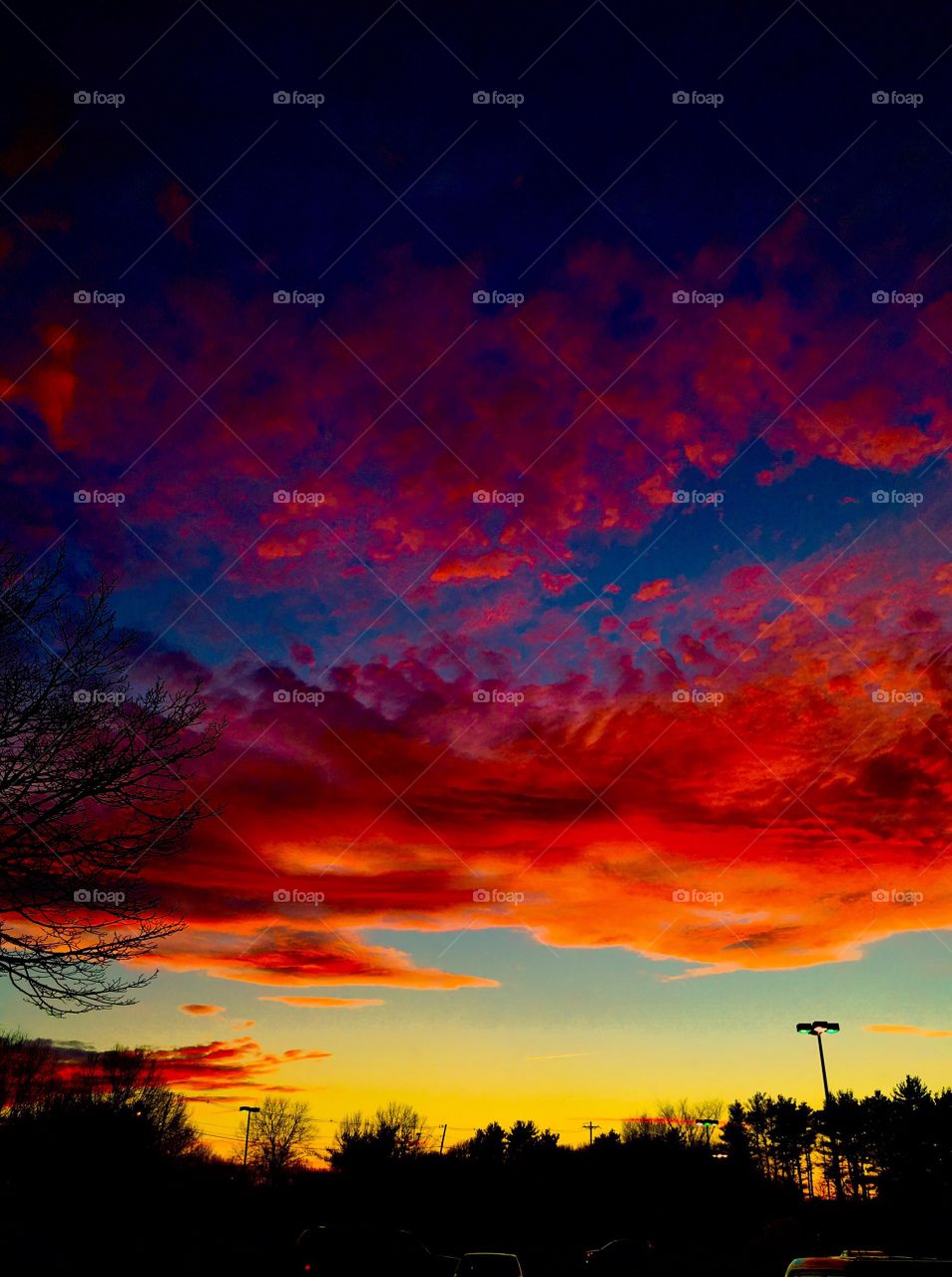Fiery red sunset sky with bold red clouds, atop layers of dark blue, orange, yellow and green  
