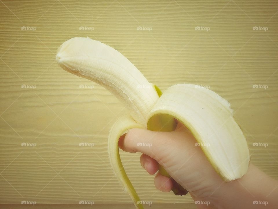 Hand Holding a Peeled Banana on a Yellow Background