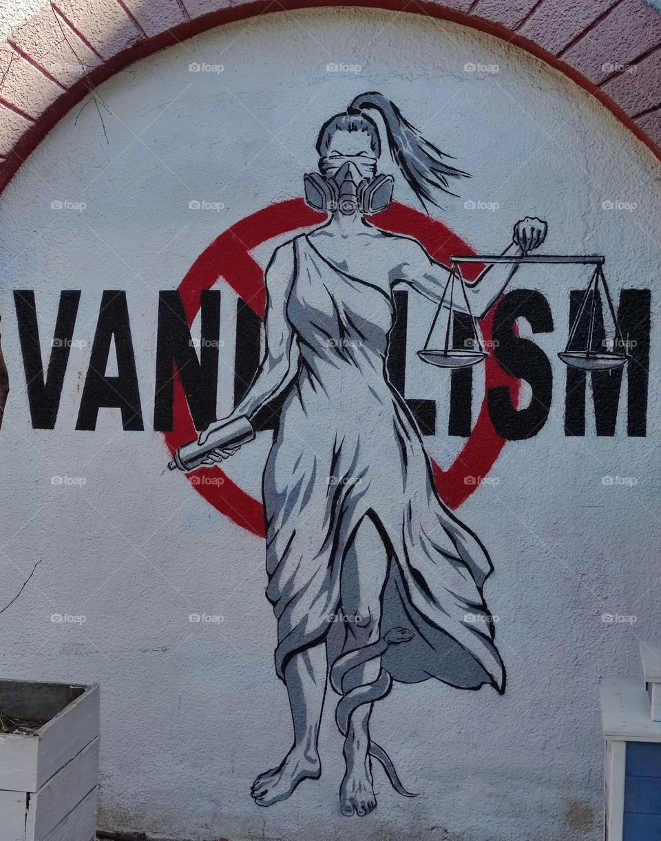 Disgust. Graffiti. A woman with a mask on the lower part of her face is painted on the wall. The woman holds the scales of justice in her hands. In the background of the woman is written in large print: "VANDALISM". Emotions against vandalism