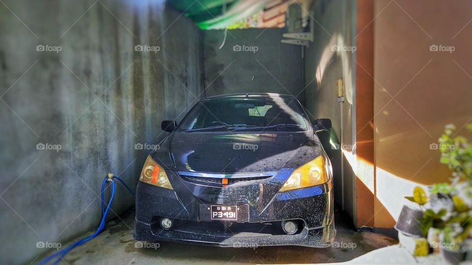 A black modern car covered with dust kept in the garage for cleaning and sunlight has fallen into car body