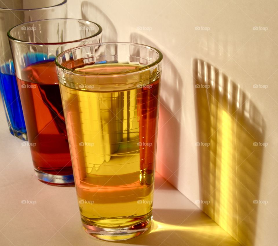 Colored water in three glasses casting colorful shadows on the wall