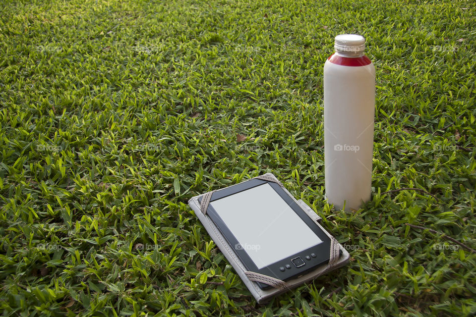 Electronic book, E-Book and a bottle of water on the green grass