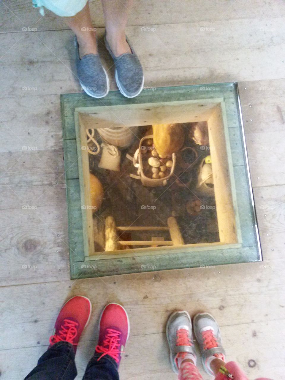 Looking down. Three pairs of feet, near a window into the floor. 