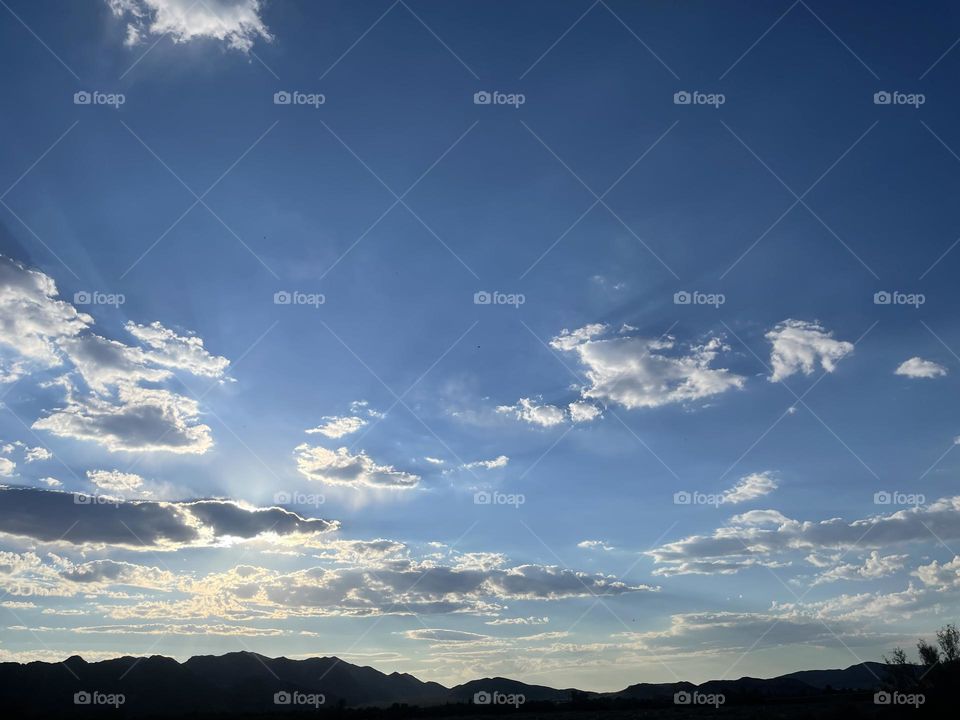 A partly cloudy sky with mountains and the sun shining. 