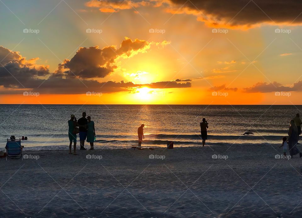 Beachcombers gather around the setting sun drinking in the memories from their Florida vacation.