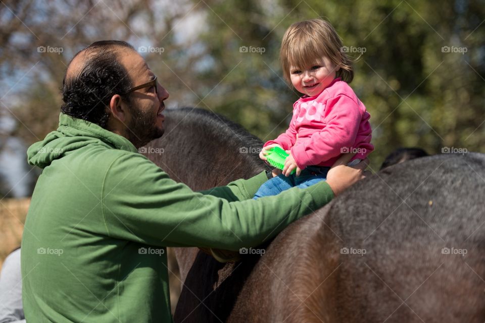 baby girl on a horse and her dad standing beside her