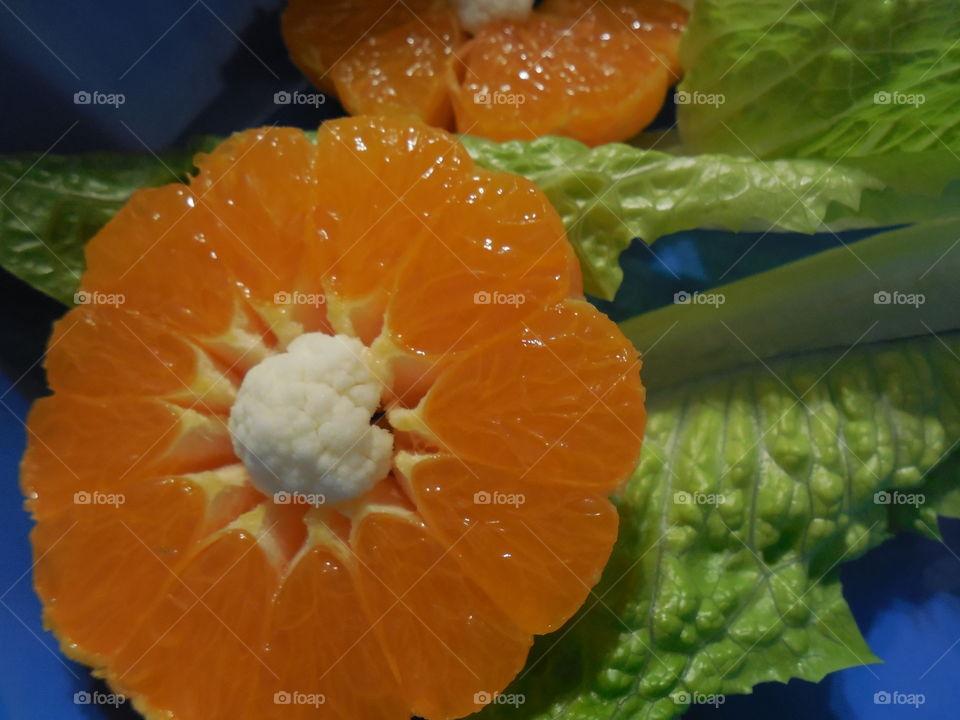 Orange Clementine flowers with cauliflower centers romaine lettuce leaves blue background
