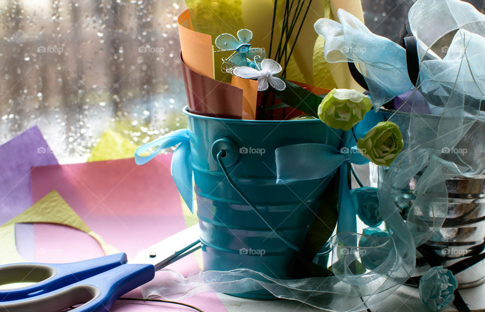 Rainy day arts and crafts materials in the window with scissors, ribbon, paper of different textures to make paper flowers and personalized cards in spring or summer theme