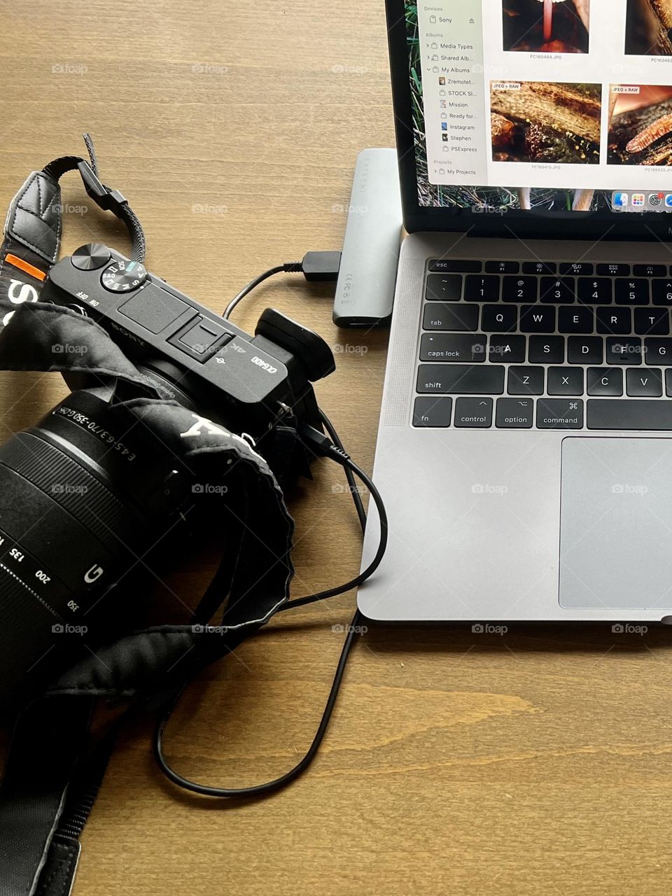 Photography workspace on wooden drafting table. Camera is plugged into laptop and a metal round container holds equipment