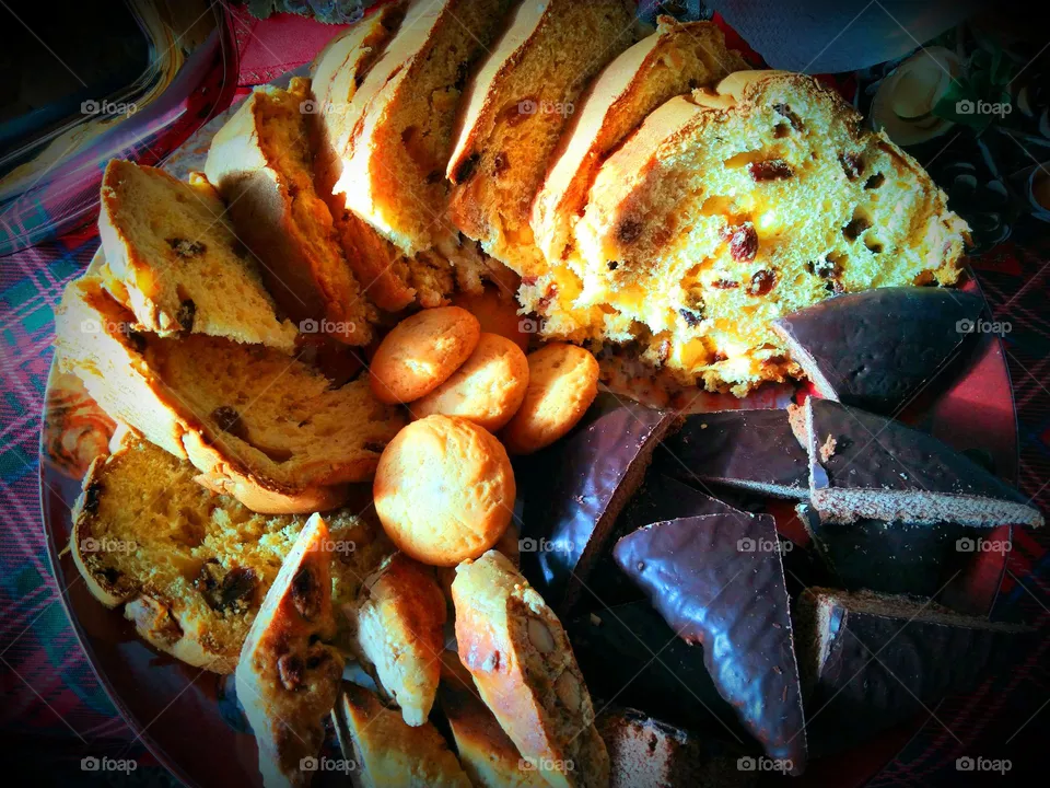 A platter full of Italian Christmas specialties: slices of panettone with raisin ans candied fruit, mostaccioli choccolate biscuits, lemon cookies and roccocò