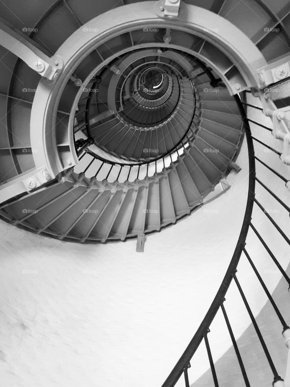 A black and white photo of the steep spiral staircase of the Ponce Inlet Lighthouse taken from below.