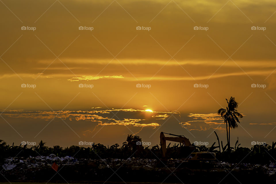 Sunset the evening light through the clouds and the shadow of Backhoe loaders On a pile of garbage.