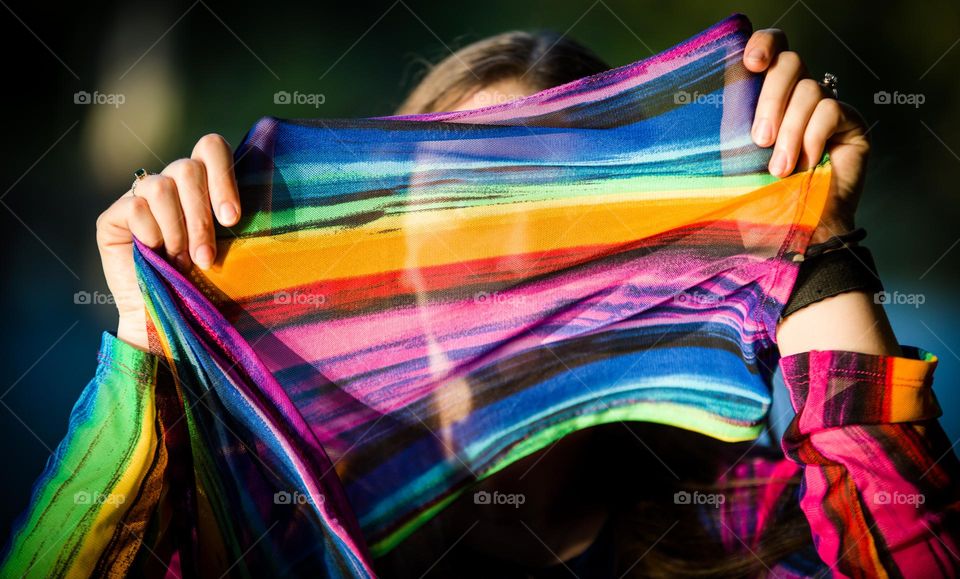 Female holding colorful rainbow scarf material in front of her face