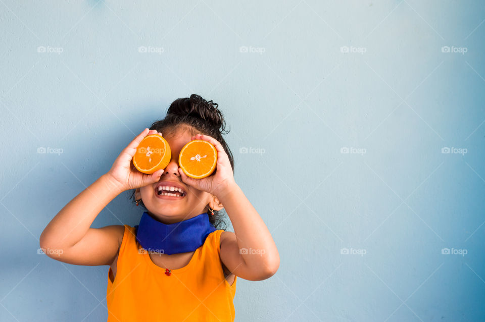 Portrait of Young girl smiling and holding halves of orange at her eyes.