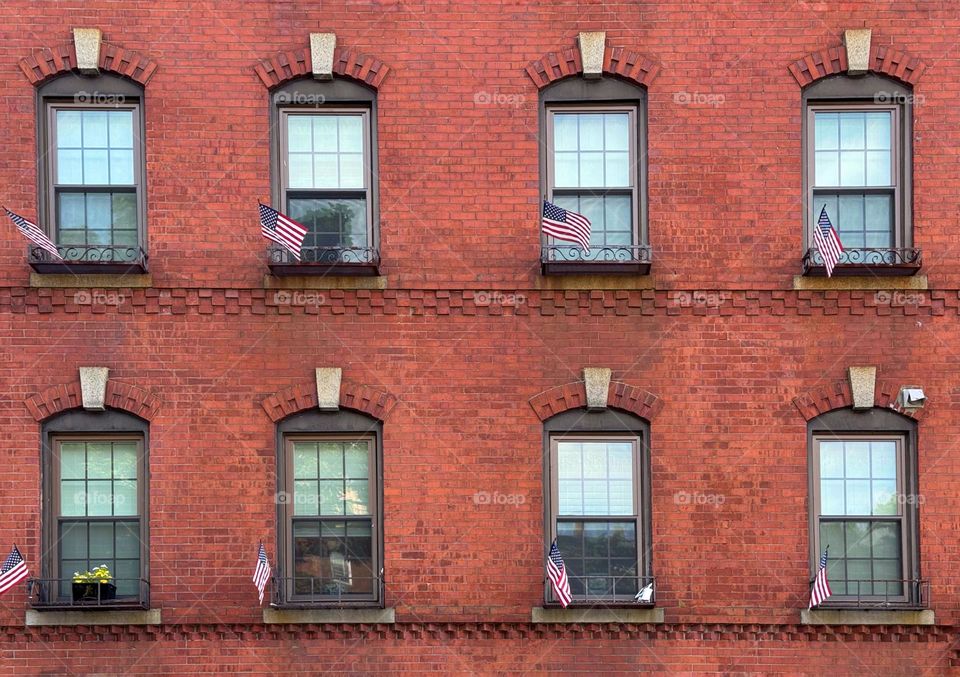 Two rows of windows on a brick building in Boston with American flags on their windowsills