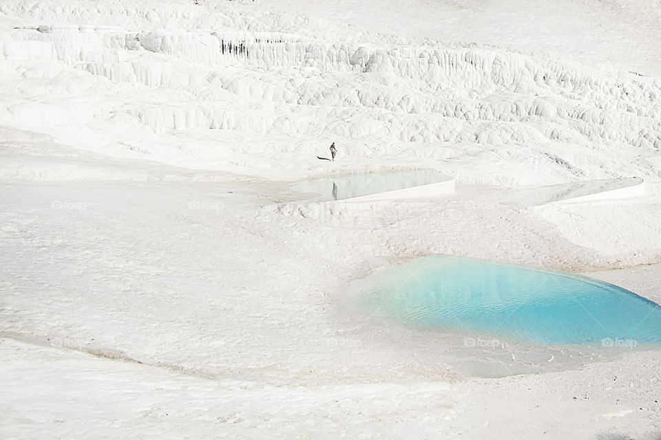 Tiny human standing on the white chalk mountain with blue lagoons, minimal concept 