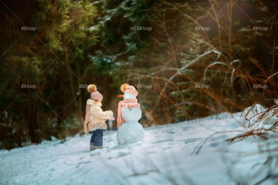 Little girl with snowman in winter park