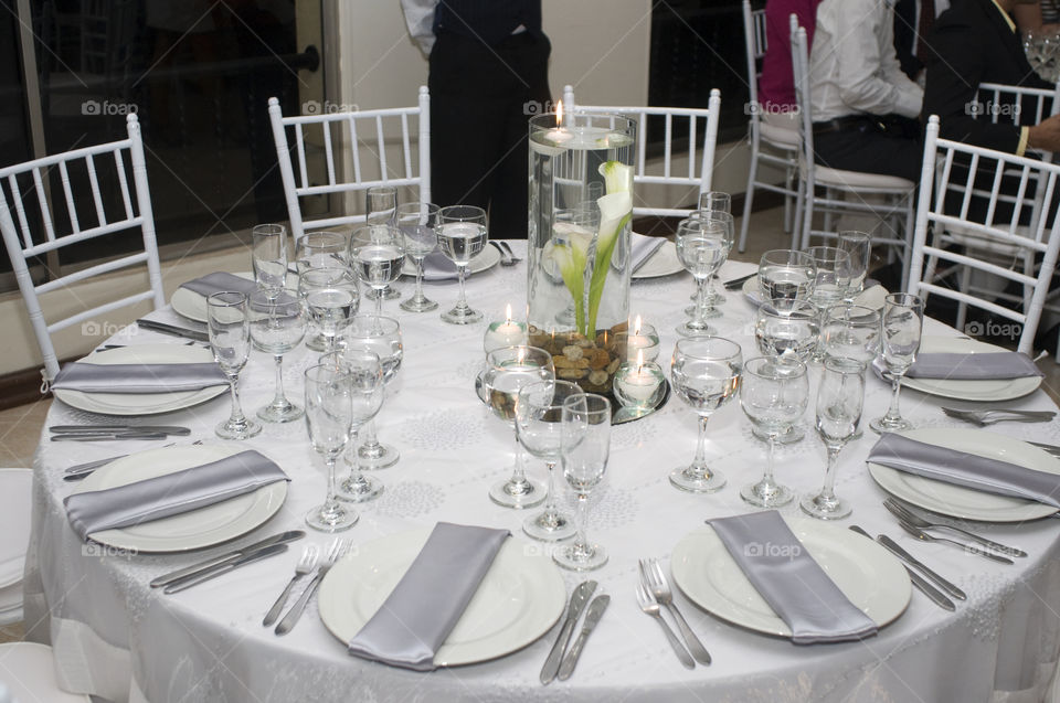 Dishes decorated table spoons forks glasses of water tablecloth chair .