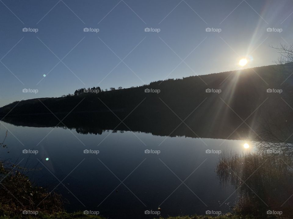 Bright sun set, disappearing behind hillside and still river. 