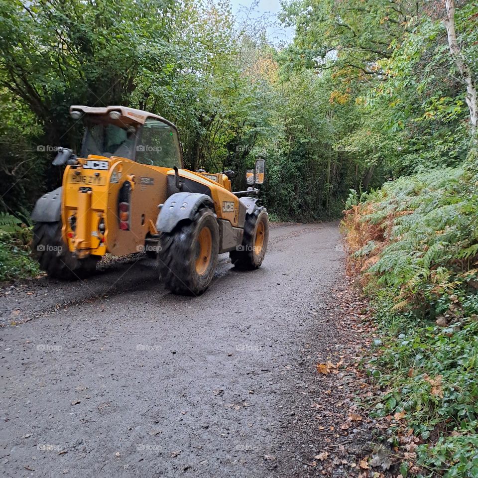 Yellow tractor driving down a country lane in U.K on an autumn afternoon. leaves and foliage surrounds.