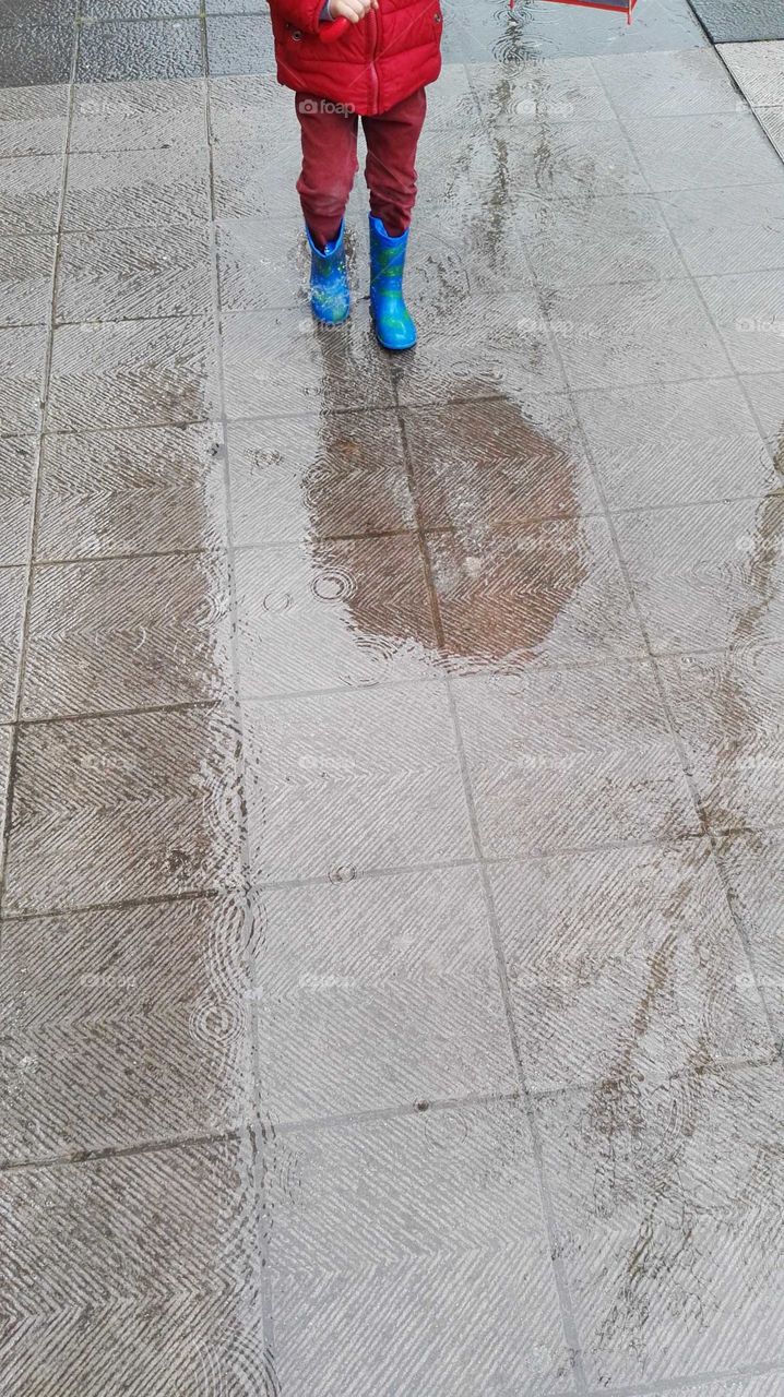 a child walking with boots and one umbrella on a wet street