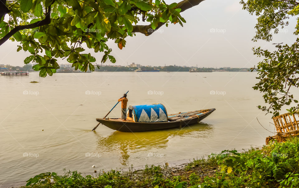 A boatman rowing Old wooden boats at the lake bank in Hooghly River Kolkata , sunny day, captured in landscape style, traavel and transportation concept. may be used background or wall paper