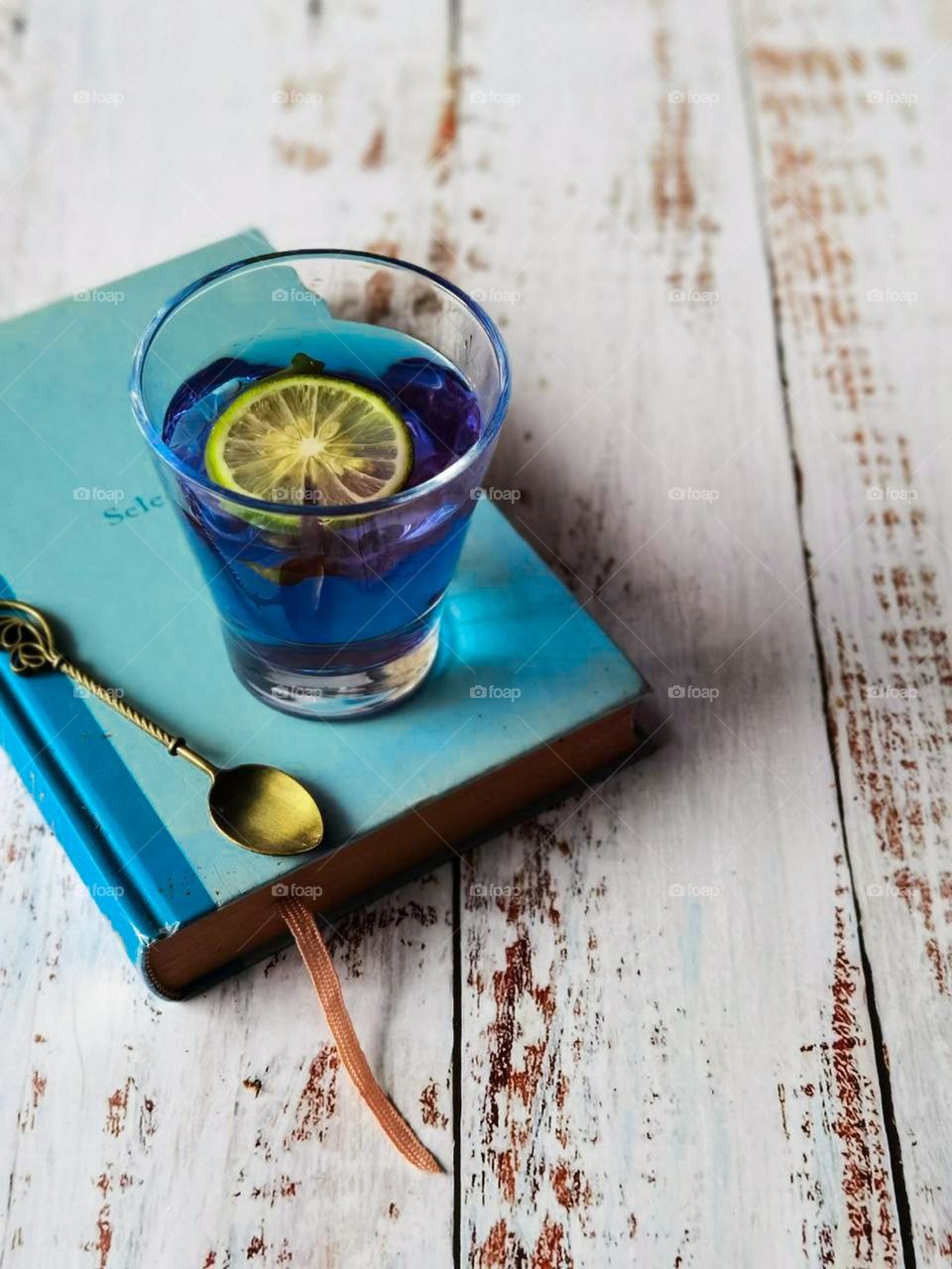 Butterfly pea flower tea with a slice of lemon. Blue hot tea on top of a blue book on a wooden white table