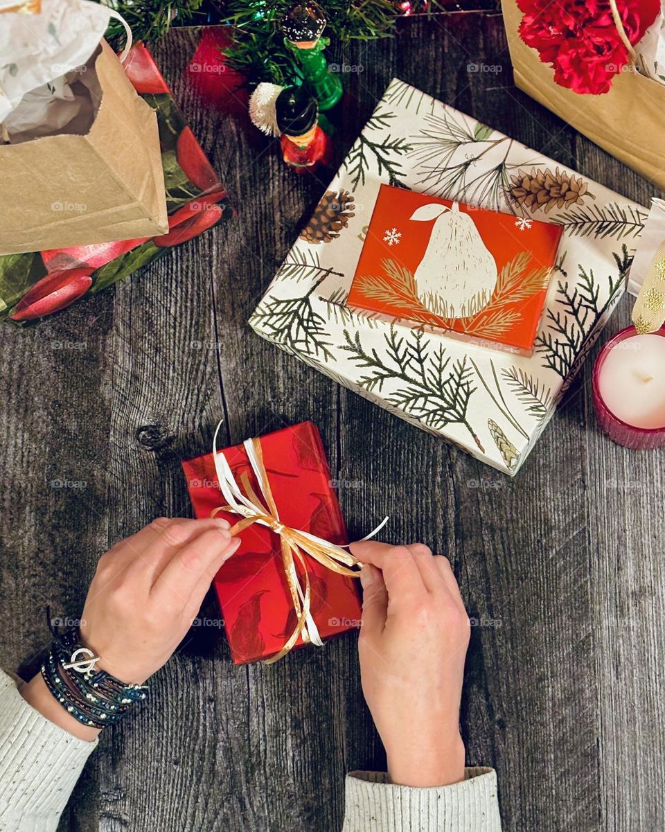 Wrapping gifts for Christmas, female hands, tying a bow. Red wrapping paper.