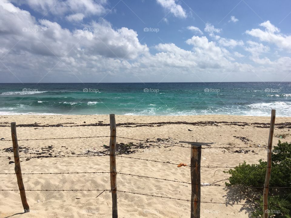 Fenced beach In Cozumel Mexico, white sand beach and barbed wire fence with clear crisp ocean in the background 