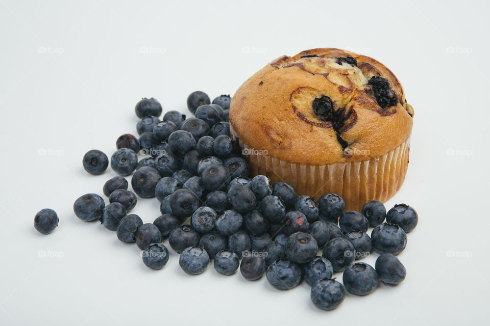 Scattered blueberries around a blueberry muffin on white background