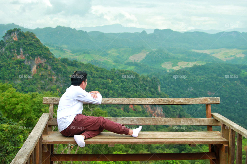 A man sitting on a bench  See the natural scenery, forests, mountains, very beautiful and happy to relax on his holiday.