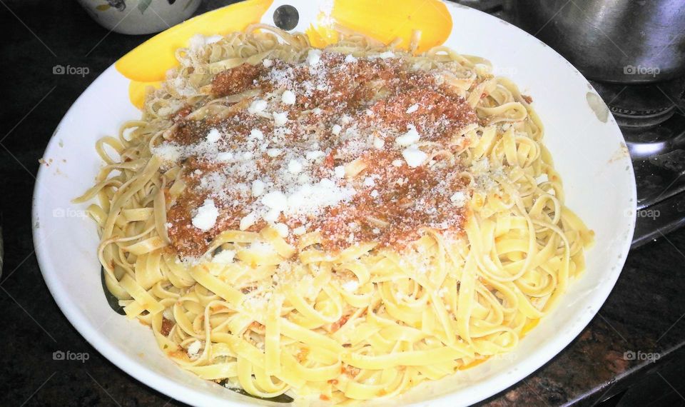 Tagliatelle pasta with bolognese tomato sauce covered with Grana Padano