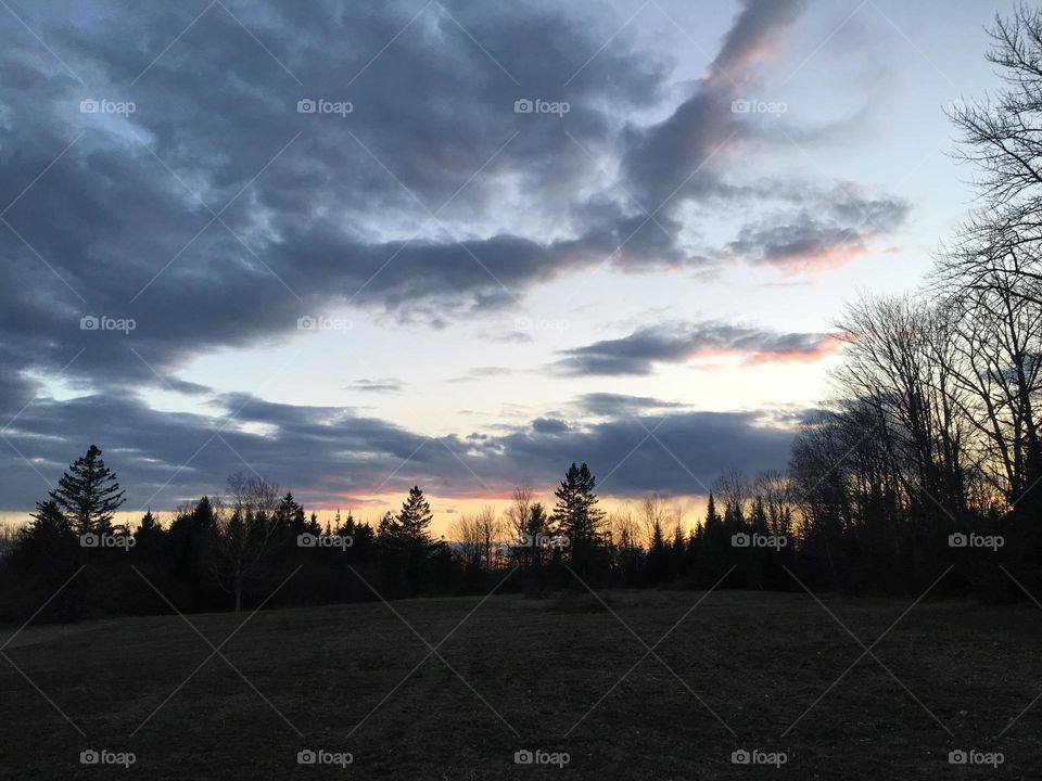 Autumn Sunset in Maine. Dark blue clouds, peach horizon and shadowed tree line.