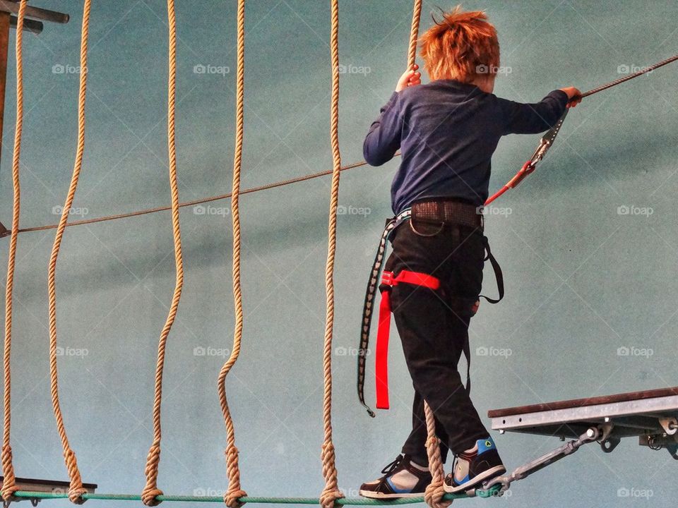 Meeting The Challenge. Young Boy Traversing A Rope Bridge
