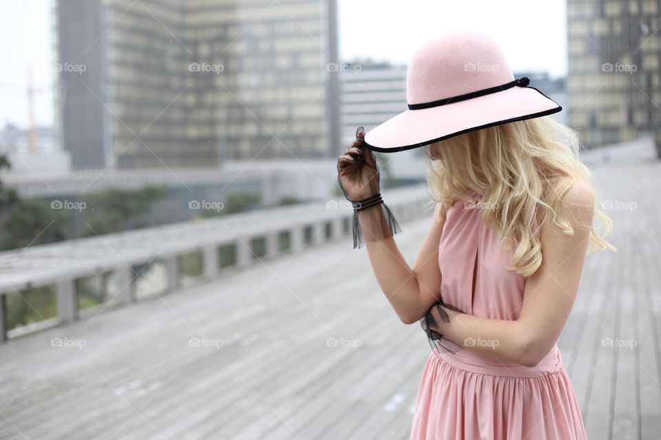 Faceless blonde girl in the pink hat and dress on the street 