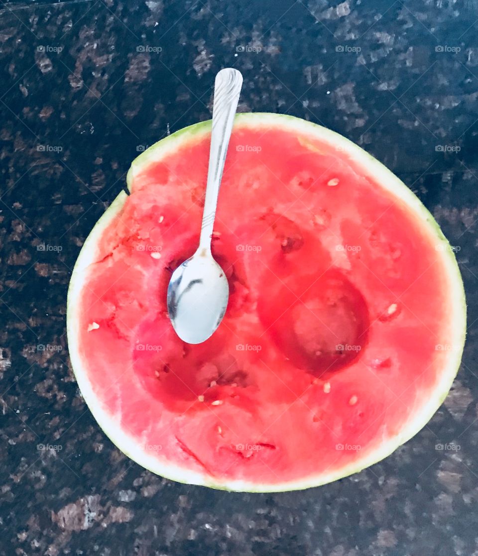 Beautiful juicy red tasty watermelon sitting on a dark granite countertop with a silver spoon ready to be eaten